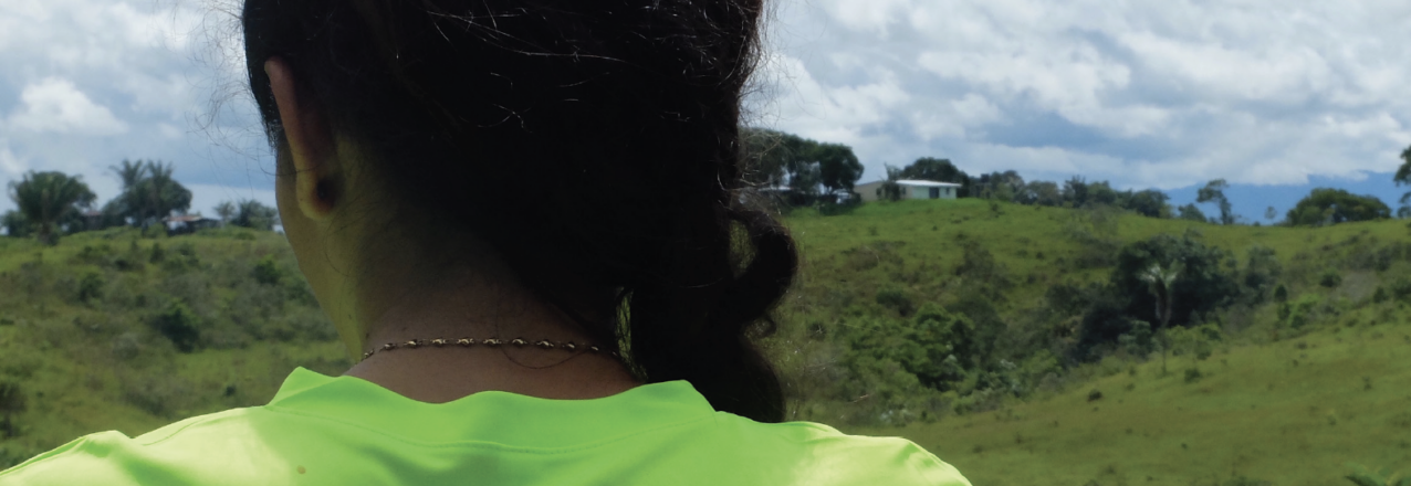 A woman in a neon green shirt faces away from the camera. The back of her shirt says "Promuevo y defiendo los derechos humanos" (Promoting and defending human rights)