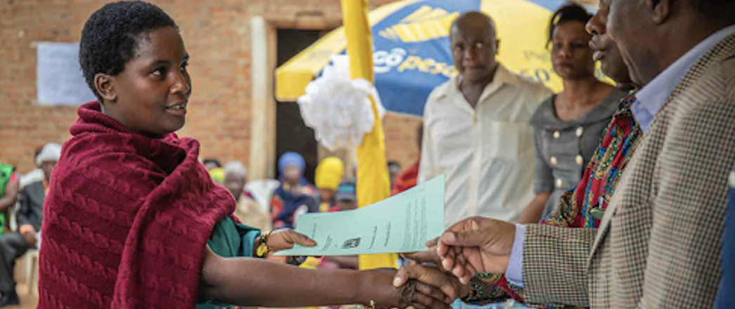 A woman shakes a man's hand as she is being handed a document.