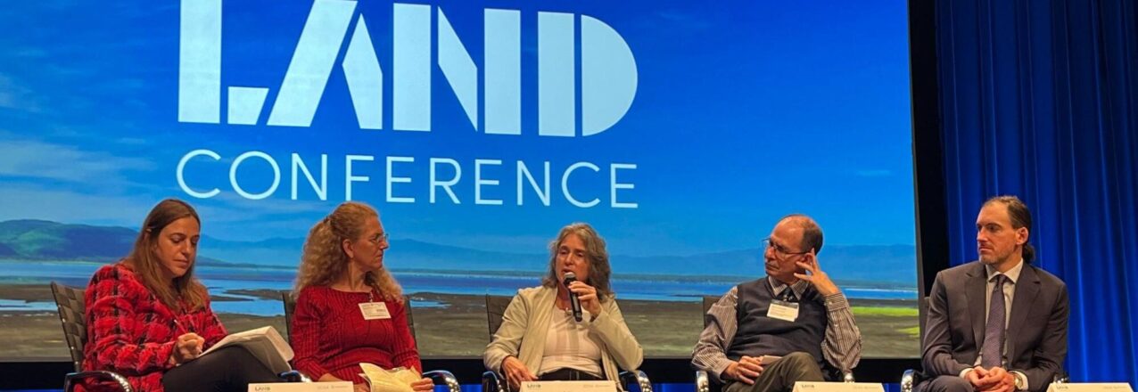 Several people participating in a panel sit in front of a large screen that states "World Bank Land Conference"