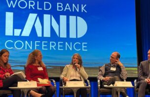 Several people participating in a panel sit in front of a large screen that states "World Bank Land Conference"