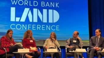 Several people participating in a panel sit in front of a large screen that states "World Bank Land Conference"