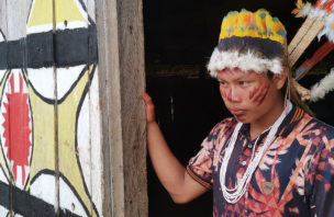 an indigenous man adorned with traditional jewelry, face paint, and head dress